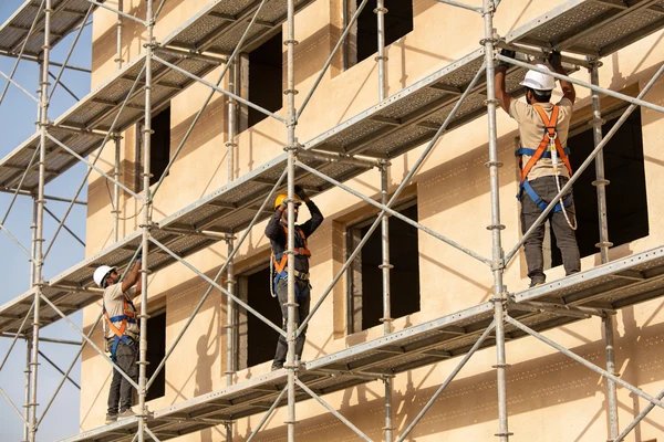 Workers assembling scaffolding on building in Oman